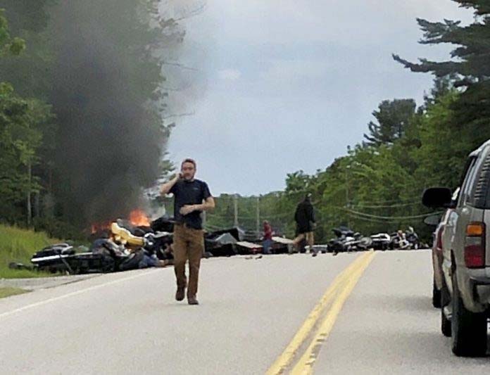 This photo provided by Miranda Thompson shows a man talking on his cellphone at the scene where several motorcycles and a pickup truck collided on a rural, two-lane highway Friday, June 21, 2019 in Randolph, N.H.  (Miranda Thompson via AP)